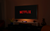 A very dark room with the Netflix wordmark shown on the background of a mounted TV with the TV having a backlight underneath