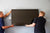 Two men installing a flat screen tv on a gray wall.