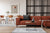 Rust colored contemporary velvet couch in front of a wall with black metal panes and a small dining area to the left.